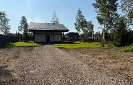 Небольшой загородный дом с тёмной крышей и гравийной подъездной дорожкой на фоне берёз