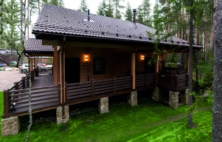 Деревянный дом-баня с широкой верандой на каменных опорах в сосновом лесу